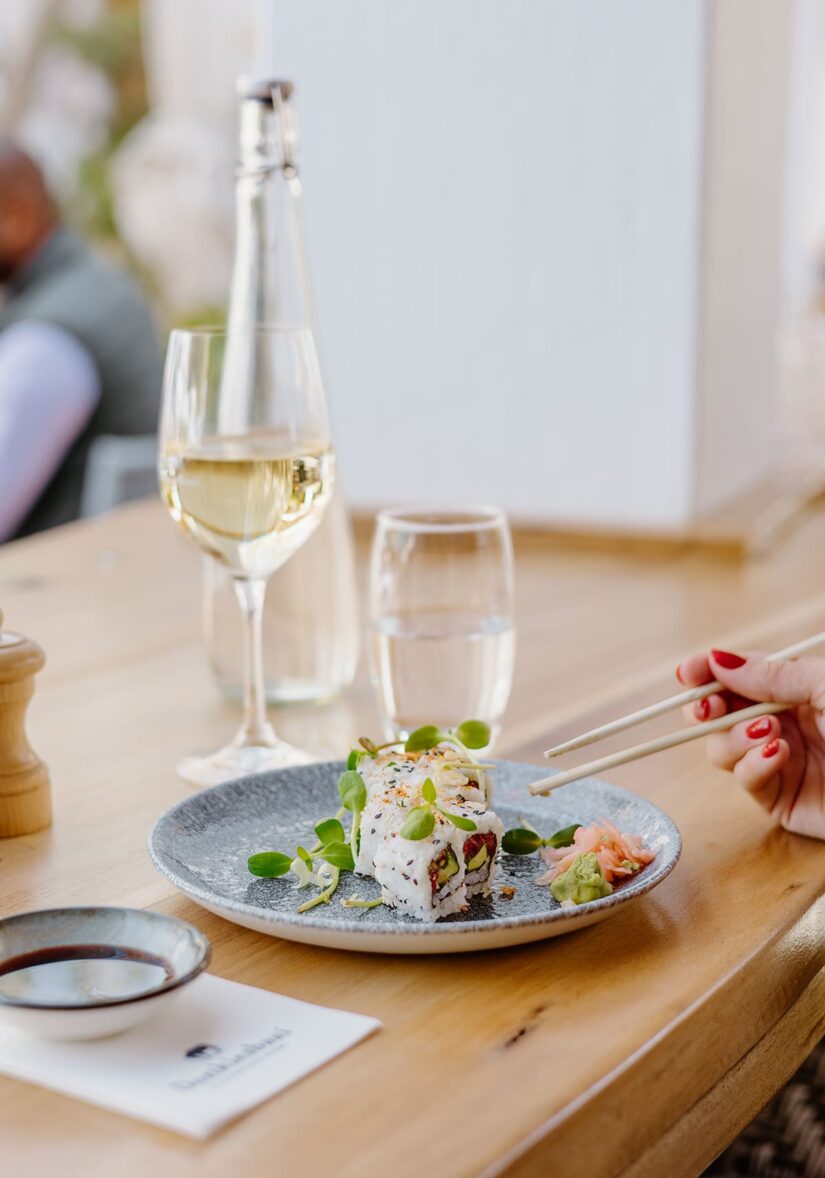 Sushi on a plate with chopsticks, glass of wine, and water.